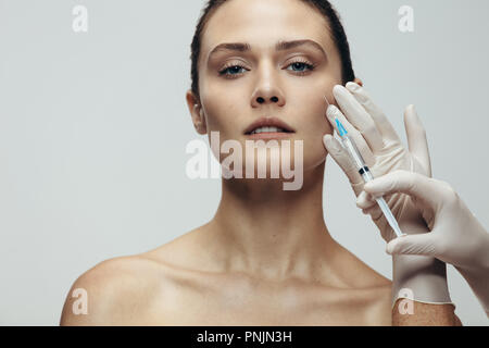 Donna getting anti rughe trattamento estetico sulla faccia da medico cosmetici. Modello femminile riceve iniezione sul suo viso da estetista su sfondo grigio Foto Stock