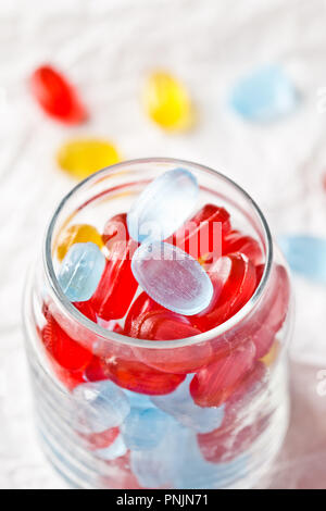 Caramelle colorate in un barattolo di vetro closeup sul libro bianco sullo sfondo Foto Stock