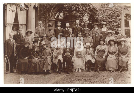 Primi del novecento seppia cartolina del gruppo di nozze con la sposa e lo sposo. La sposa e le sue damigelle hanno sono holding mazzi di fiori, al di fuori di casa grande, circa 1919, U.K. Foto Stock