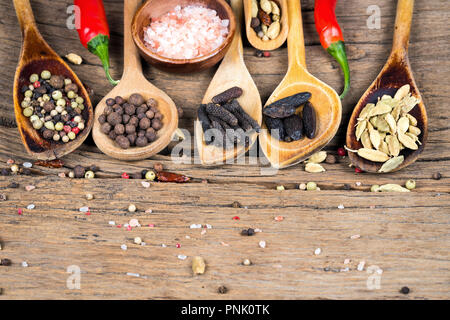 Close-up di legno cinque cucchiai di cottura con varie spezie esotiche e due peperoncino rosso e una ciotola di legno di rosa con cristalli di sale su un rustico woode Foto Stock