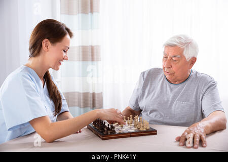 Giovani femmine custode giocando a scacchi con il Senior uomo a casa Foto Stock