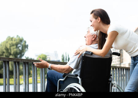 Giovane donna con il suo padre disabili vicino alla ringhiera all'aperto Foto Stock