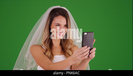 Bella giovane sposa tenendo selfie con lo smartphone su schermo verde Foto Stock