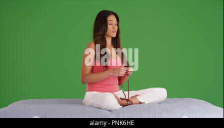 Latina spirituale seduta zampe croce meditando con talloni su schermo verde Foto Stock