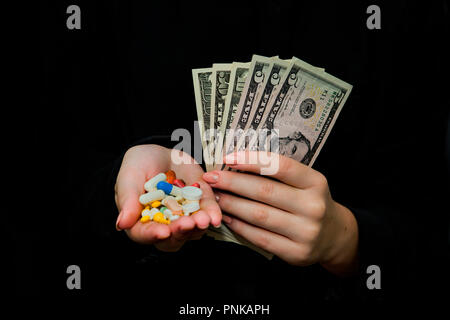 Il denaro e le pillole in mani, isolati su nero. Sprecando troppo denaro sul farmaco. La tossicodipendenza concetto Foto Stock