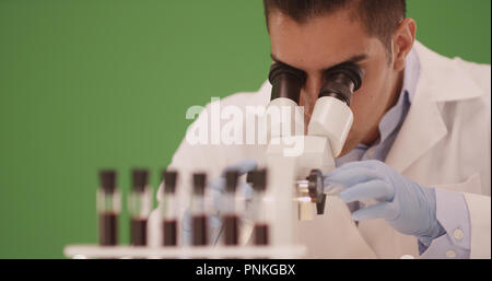 Ispanico medical research scientist in laboratorio mediante microscopio su schermo verde Foto Stock