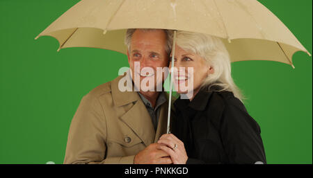 Felice coppia di anziani in piedi sotto la pioggia con un ombrello su schermo verde Foto Stock