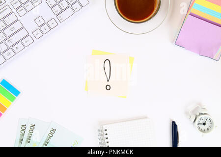 Un punto esclamativo sull'adesivo è una nota su un desktop bianco accanto a una tazza di caffè e una tastiera. Vista superiore, disposizione piatta Foto Stock