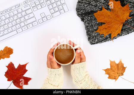 Caffè con marshmallow in mani su un desktop bianco accanto a un blocco vuoto e tastiera, foglie di autunno. Caduta dell'umore. Vista superiore, disposizione piatta. Copiare la spa Foto Stock