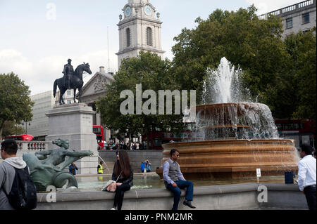 Primo piano di turisti rilassante sulla parete di Mermaid statua e fontana, Trafalgar Square con la statua equestre di Giorgio IV in background, Foto Stock