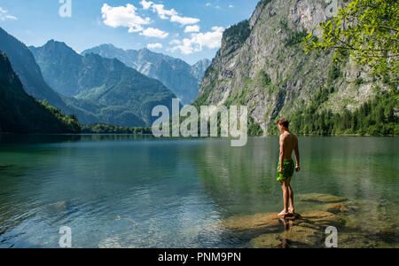 Giovane uomo sorge su una pietra nel lago Obersee, dietro Watzmannmassiv, Salet am Königssee, Parco Nazionale di Berchtesgaden Foto Stock
