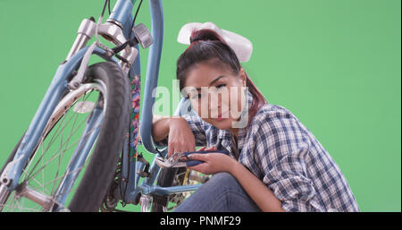 Asian donna sorridente e fissa la sua moto su schermo verde Foto Stock