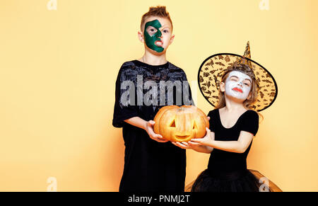 Bambini Un ragazzo e una ragazza in diversi costumi di Halloween ringhiando e spaventare la fotocamera con la zucca isolato su sfondo giallo. Foto Stock