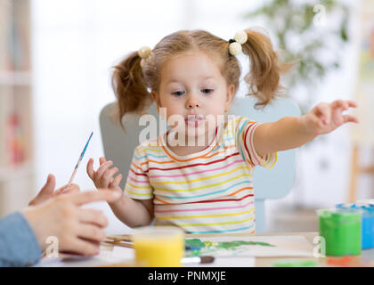 Carino piccolo bimbo ragazza in camicia a righe e pony tails vernici nella classe d'arte Foto Stock