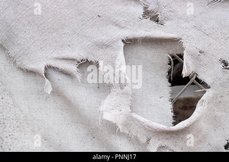 Bianco sporco grigio grunge lacerato tessuto vintage canvas texture di sfondo, con la maglia di catena visto attraverso un foro, bordi sfrangiati Foto Stock