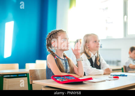 Un gruppo di bambini della scuola di tutti alzando le mani in aria per rispondere Foto Stock