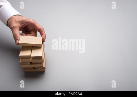 Imprenditore mano facendo una pila di picchetti di legno in una immagine concettuale della visione aziendale e start up con il grigio spazio copia. Foto Stock