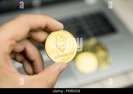 Imprenditore maschio mano azienda Ethereum moneta su uno sfondo di tastiera portatile e la pila di monete d'oro. Denaro virtuale e la crescita finanziaria concetto. Trading di Data Mining Ethereum. Foto Stock