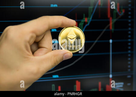 Imprenditore maschio mano azienda Ethereum moneta su uno sfondo del grafico di crescita su uno schermo di computer portatile. Denaro virtuale e la crescita finanziaria concetto su sfondo grafico. Trading di Data Mining Ethereums. Foto Stock