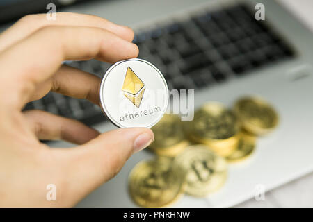 Imprenditore maschio mano azienda Ethereum moneta su uno sfondo di tastiera portatile e la pila di monete d'oro. Denaro virtuale e la crescita finanziaria concetto. Trading di Data Mining Ethereum. Foto Stock