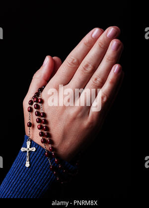 Mani femminili pregando tenendo un rosario perline con Gesù Cristo in croce o Crocifisso su sfondo nero. Donna con cristiana religiosa cattolica fa Foto Stock