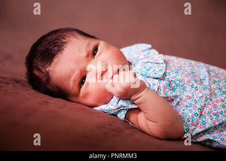 Close up ritratto di un simpatico due settimane bambino neonato bambina coricata, apre gli occhi e si guarda intorno indossa un abito floreale Foto Stock