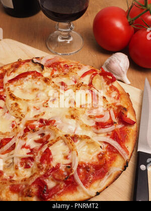 Una gustosa pizza su un rustico di legno con un bicchiere di vino rosso Foto Stock