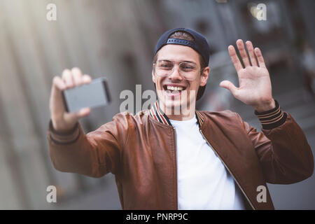 Selfie mania! Eccitato giovane ragazzo sta facendo selfie su una telecamera. Egli indossa casual usura alla moda e ritornano a scatto Foto Stock