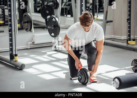 Uomo muscolare mettendo le piastre pesanti su barbell durante gli allenamenti in palestra Foto Stock