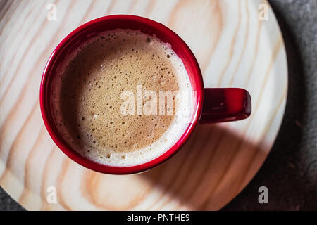 Rosso la tazza con il caffè con il latte sul round vassoio in legno Foto Stock