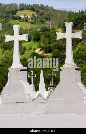 Asturias, Spagna. Pietra Bianca attraversa in un cimitero con un villaggio di montagna in background. Foto Stock