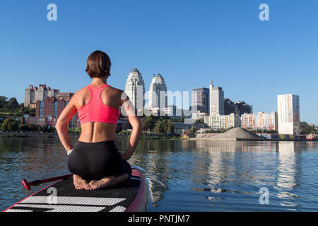 Donna seduta la pratica di variazione di yoga pone sulla scheda pala Foto Stock