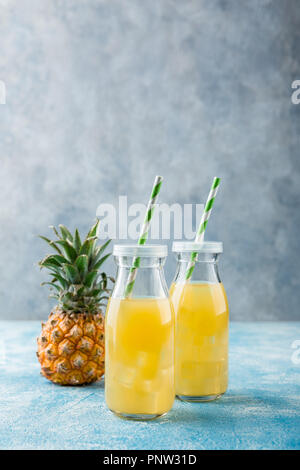 Ananas cocktail o succo in due bottiglie di vetro con cannucce con ghiaccio e due mini ananassi su uno sfondo blu Foto Stock