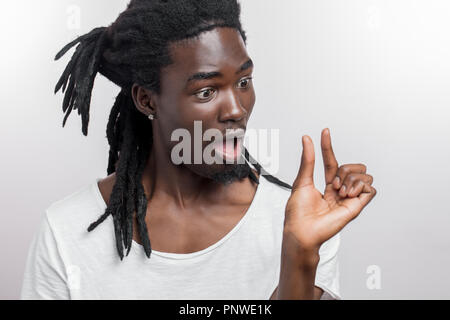 Sorpreso maschio africana con dreadlocks mostra un piccolo segno con la mano Foto Stock