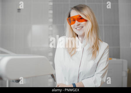 Donna bionda dentista in bianco uniforme seduto accanto per apparecchiature dentali. Foto Stock
