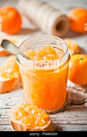 Orange inceppamento in un barattolo di vetro, tangerini e pane rustico tavolato in legno Foto Stock