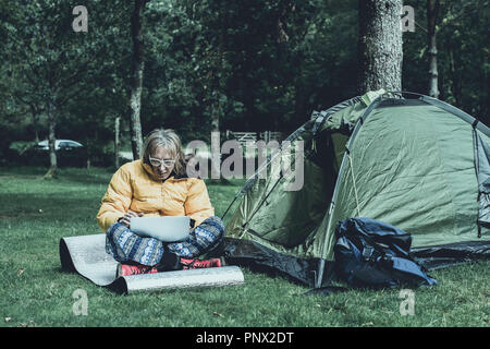 Casualmente vestito uomo al lavoro sul suo laptop, sul campeggio nelle zone rurali del Regno Unito.Accesso internet mobile consentendo alle persone di lavorare in posizione remota. Foto Stock