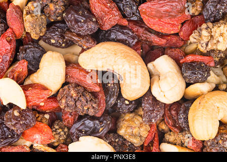 Miscela di anacardi semi e dolce di frutti di bosco essiccati close-up. Tostate pila, secco gelsi, uvetta e goji frutti. Decorativo-marrone rossastro texture. Foto Stock