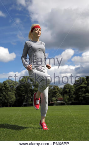 Donna bionda in una tuta in esecuzione sul posto e excercising nel parco Foto Stock