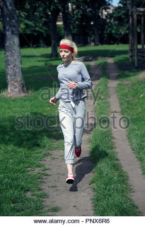 Donna bionda in una tuta in esecuzione e excercising nel parco Foto Stock