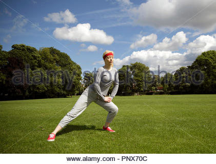 Donna bionda in una tuta di eseguire esercizi di stiramento nel parco Foto Stock