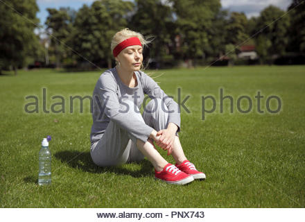 Donna bionda in una tuta excercising e seduta nel parco Foto Stock