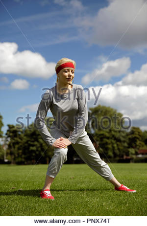 Donna bionda in una tuta di eseguire esercizi di stiramento nel parco Foto Stock