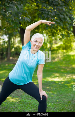 Ritratto di donna senior facendo esercizi streching nel parco Foto Stock