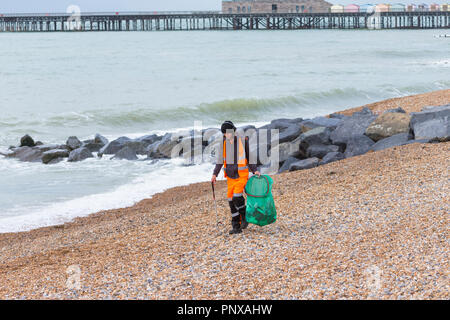 Giovane Uomo con cuffie di prelevare i rifiuti e la pulizia della spiaggia vestito in arancione Kier Azienda di abbigliamento, Hastings, east sussex, Regno Unito Foto Stock