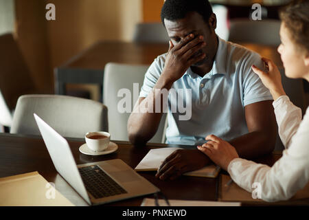 Giovane imprenditore in problemi di condivisione del suo problema con il collega di sesso femminile che consolante di lui Foto Stock