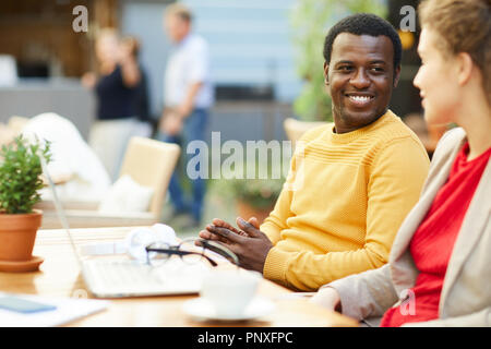 Due giovani colleghi interculturale in seduta outdoor cafe e discutere di momenti di lavoro Foto Stock