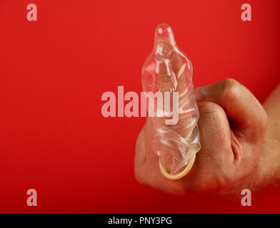 Close up man mano che mostra protesta o insulto gesto maleducato con lattice preservativo sul dito su sfondo rosso con copia spazio, basso angolo vista laterale Foto Stock