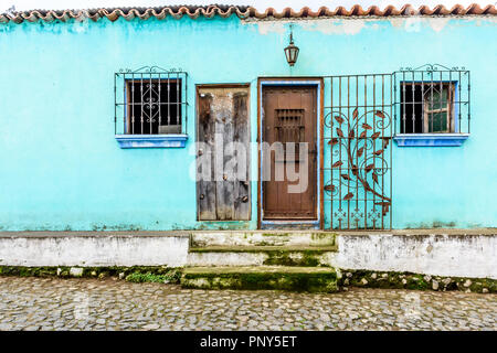 Il turchese dipinto esterno della casa con decorazioni in ferro battuto su windows & porta in strada di ciottoli in Guatemala, America Centrale Foto Stock