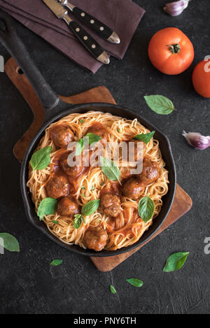 Gli spaghetti con le polpette di carne, salsa di pomodoro e basilico fresco in ghisa pan. In casa sani piatti di pasta italiana rustico sfondo nero con copia spa Foto Stock